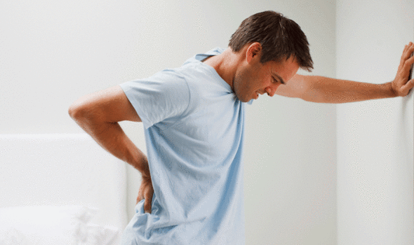 Man with Back Pain Proping Himself up on a Wall